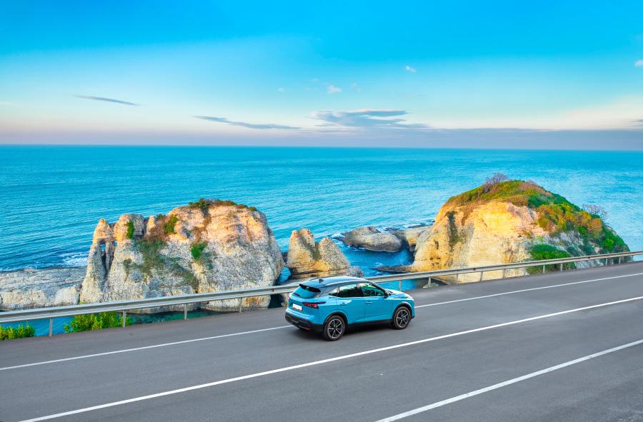 Une voiture de location longe une route côtière offrant une vue sur la mer et des falaises, idéale pour découvrir la destination à son rythme.